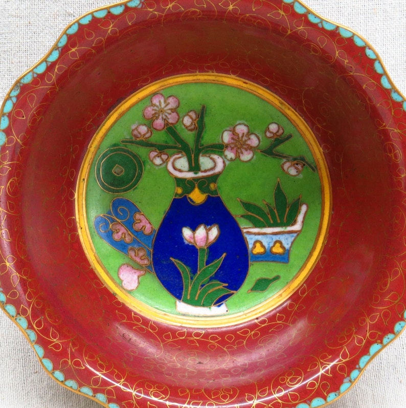 May include: A red and gold cloisonn&eacute; bowl with a blue and green floral design. The bowl has a scalloped edge and is decorated with a floral pattern.
