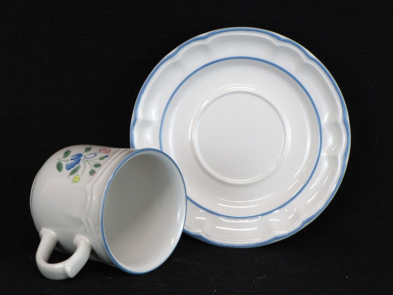 May include: A white ceramic teacup and saucer with a blue and floral design. The cup has a handle and the saucer has a scalloped edge.