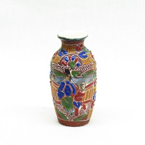 May include: A small, brown ceramic vase with a white rim. The vase is decorated with colourful, intricate designs of people and flowers.