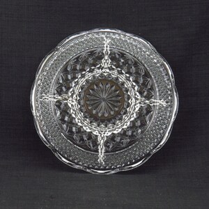 May include: A clear glass serving dish with a diamond pattern and four sections. The dish has a scalloped edge.