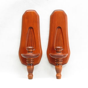 May include: A pair of wooden wall-mounted candle holders with a dark brown finish. Each holder has a simple design with a round base and a single candle holder.
