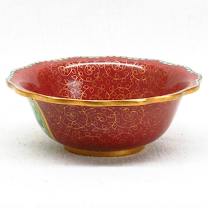 May include: A red and gold bowl with a floral pattern. The bowl has a scalloped edge and is made of ceramic.