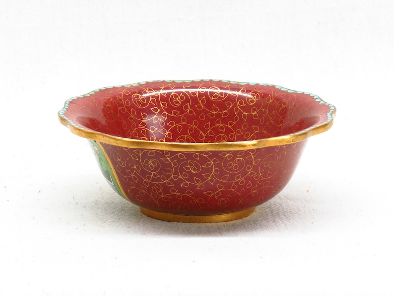 May include: A red and gold bowl with a floral pattern. The bowl has a scalloped edge and is made of ceramic.