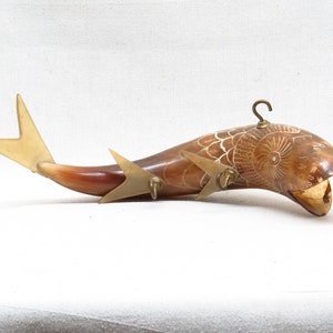 K&ouml;nnte beinhalten: Eine geschnitzte Fischskulptur aus Horn mit einem Messinghaken und einer Schwanzflosse. Das Horn ist braun und wei&szlig; mit aufwendigen Schnitzereien. Die Skulptur ist etwa 30 cm lang.