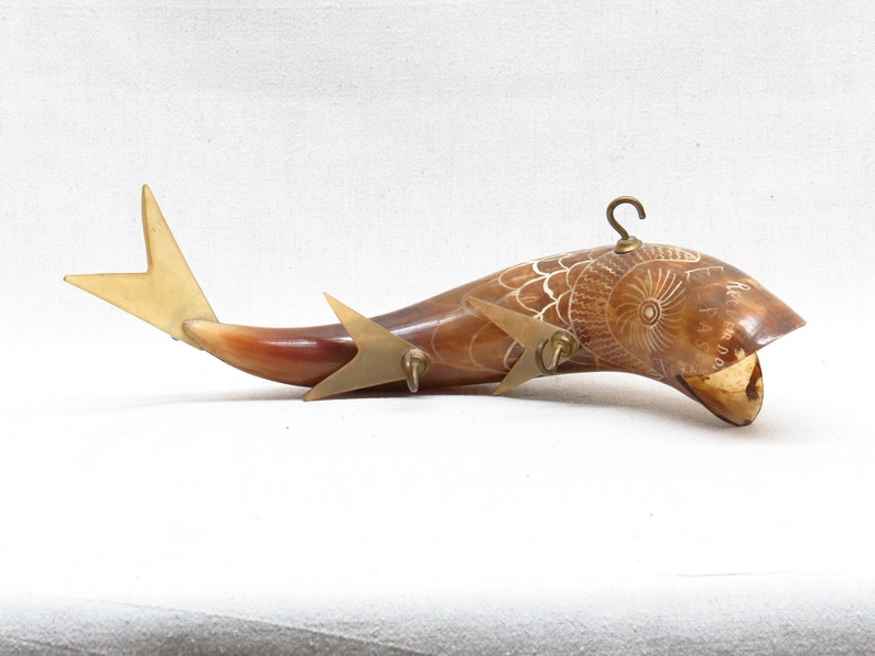 K&ouml;nnte beinhalten: Eine geschnitzte Fischskulptur aus Horn mit einem Messinghaken und einer Schwanzflosse. Das Horn ist braun und wei&szlig; mit aufwendigen Schnitzereien. Die Skulptur ist etwa 30 cm lang.