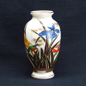 May include: A white ceramic vase with a floral design. The vase features a blue iris, green birds, and brown and green leaves on a white background.