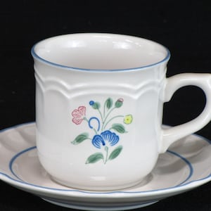 May include: A white ceramic teacup and saucer set with a blue floral design. The cup has a scalloped rim and a handle. The saucer has a blue band around the edge.