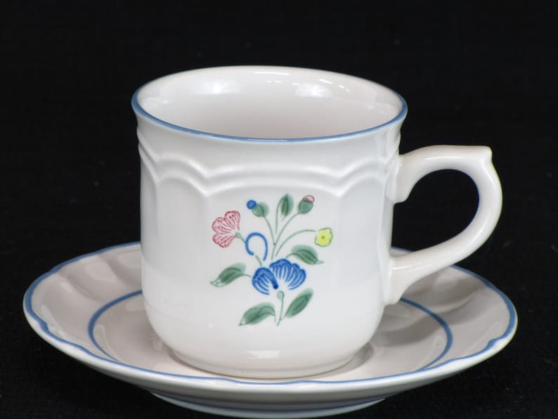 May include: A white ceramic teacup and saucer set with a blue floral design. The cup has a scalloped rim and a handle. The saucer has a blue band around the edge.