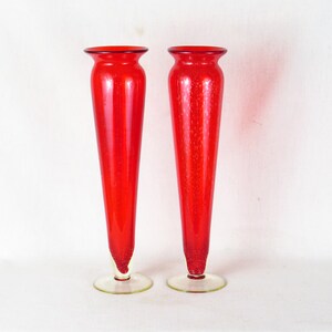 May include: Two red glass vases with a textured surface and clear glass bases.