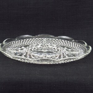 May include: A clear glass serving tray with a diamond pattern and a central divided section. The tray has a scalloped edge.