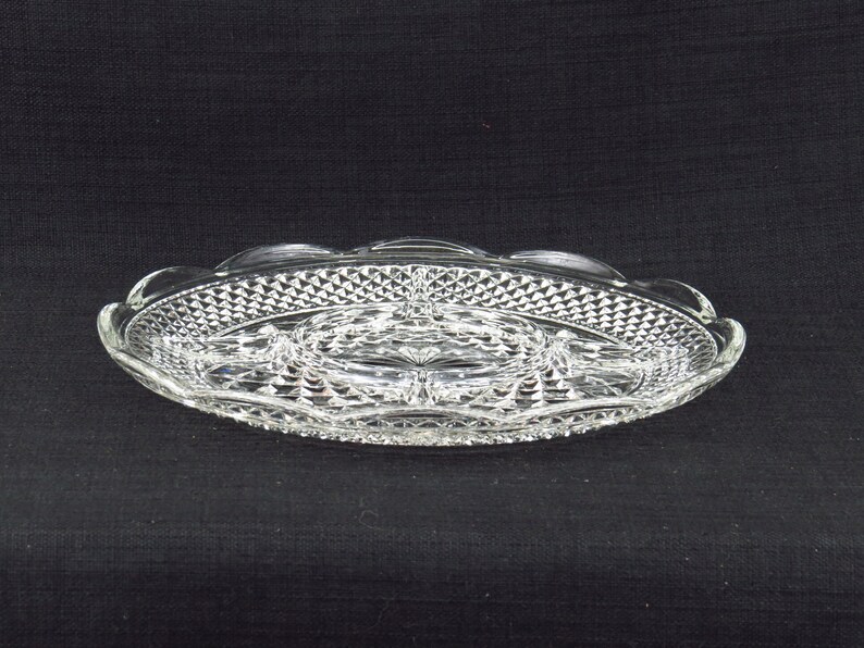May include: A clear glass serving tray with a diamond pattern and a central divided section. The tray has a scalloped edge.