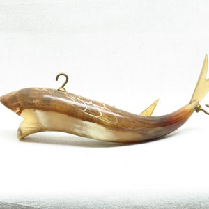 K&ouml;nnte beinhalten: Ein braunes und wei&szlig;es fischf&ouml;rmiges Hornornament mit Messinghaken an Ober- und Unterseite. Das Horn ist mit einem wei&szlig;en Muster verziert.