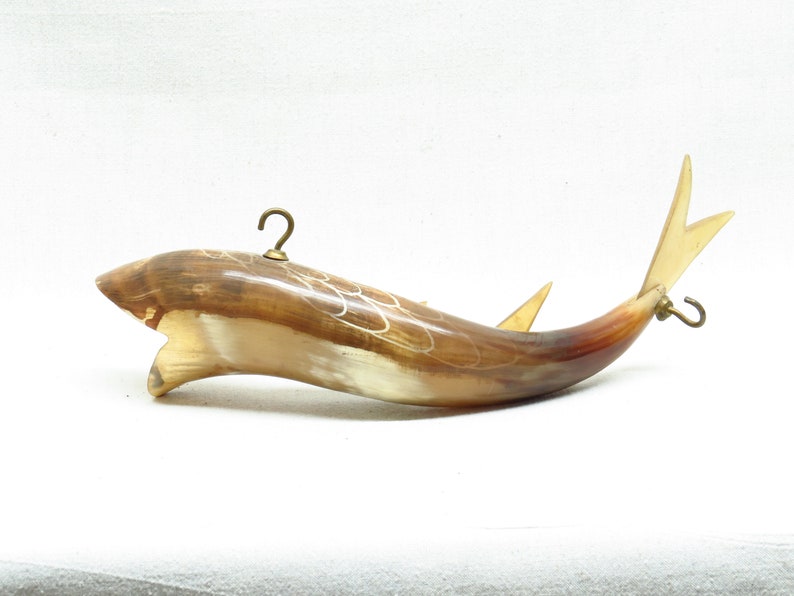 K&ouml;nnte beinhalten: Ein braunes und wei&szlig;es fischf&ouml;rmiges Hornornament mit Messinghaken an Ober- und Unterseite. Das Horn ist mit einem wei&szlig;en Muster verziert.
