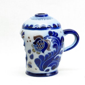 May include: A blue and white ceramic mug with a floral design. The mug has a chipped edge and a handle.