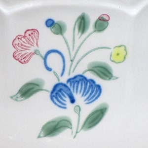 May include: A white ceramic plate with a floral design. The design features blue, pink, green, and yellow flowers.