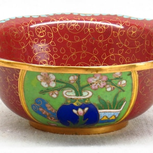 May include: A small, red and green cloisonn&eacute; bowl with a floral design. The bowl has a gold rim and a blue vase with pink flowers.