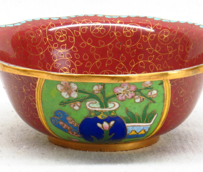 May include: A small, red and green cloisonn&eacute; bowl with a floral design. The bowl has a gold rim and a blue vase with pink flowers.