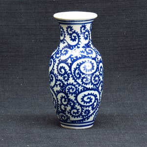 Puede incluir: Un jarrón de cerámica blanca con un patrón de espiral azul y blanco. El jarrón mide aproximadamente 25 cm de alto y tiene un cuello estrecho.
