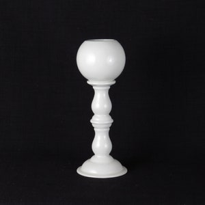 May include: A white ceramic candle holder with a round top and a tall, slender base. The holder has a smooth, glossy finish.
