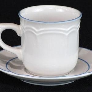 May include: White ceramic teacup and saucer with a blue trim. The cup has a scalloped design around the top.