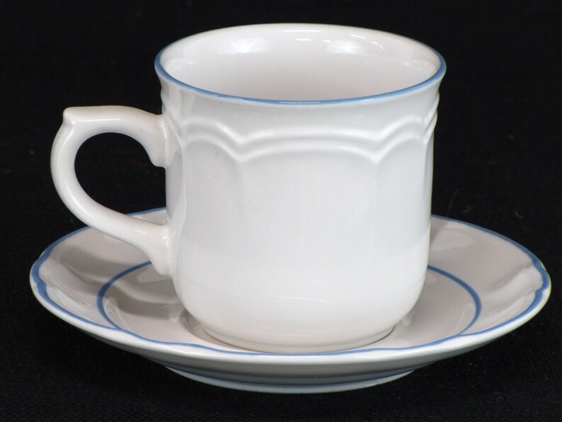 May include: White ceramic teacup and saucer with a blue trim. The cup has a scalloped design around the top.