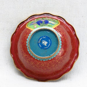 May include: Red and gold cloisonn&eacute; bowl with a blue and turquoise center. The bowl has a scalloped edge and a floral design. The bottom of the bowl has a blue sticker with the text "Cixi China Ltd. People's Republic of China."