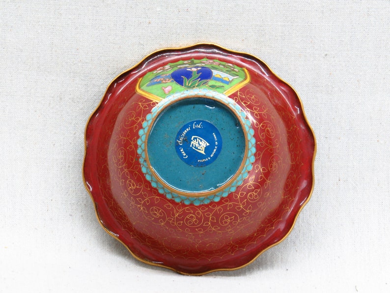 May include: Red and gold cloisonn&eacute; bowl with a blue and turquoise center. The bowl has a scalloped edge and a floral design. The bottom of the bowl has a blue sticker with the text "Cixi China Ltd. People's Republic of China."