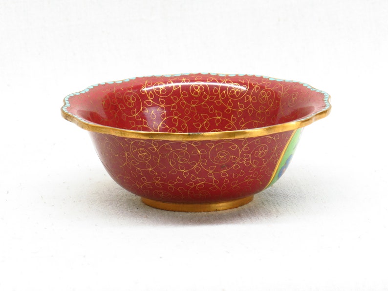 May include: A red and gold cloisonn&eacute; bowl with a scalloped rim and a floral design. The bowl is decorated with a peacock feather design on the side.