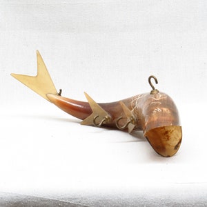 K&ouml;nnte beinhalten: Ein dekorativer, an der Wand montierter Horn mit einem Fischdesign. Das Horn besteht aus braunem und wei&szlig;em Material und hat drei Messinghaken. Der Fischschwanz besteht aus hellbraunem Material und hat eine wei&szlig;e Spitze.