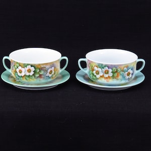 Pode incluir: Duas tigelas de sopa de porcelana branca com desenhos florais verdes e brancos e pires combinando.