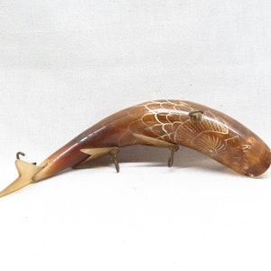 K&ouml;nnte beinhalten: Eine geschnitzte Hornskulptur eines Fisches mit einem detaillierten Design. Das Horn ist braun und das Design ist wei&szlig;. Die Skulptur ist auf einem Metallst&auml;nder mit drei Haken montiert.