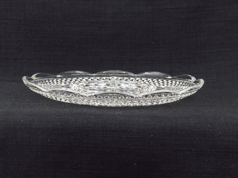 May include: A clear glass serving dish with a scalloped edge and a diamond pattern. The dish is oval shaped and has a raised centre section.