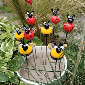 Peut inclure: Un ensemble de huit piquets de jardin en verre représentant des coccinelles et des abeilles. Les piquets sont en verre et ont une tige en fil métallique noir. Les coccinelles sont rouges avec des points noirs et les abeilles sont jaunes avec des rayures noires.