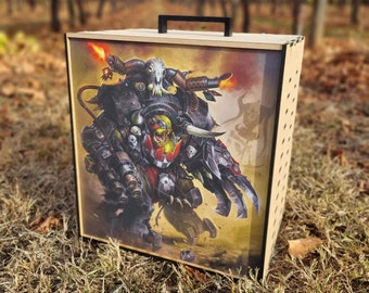 May include: A wooden box with a black handle and a colourful illustration of a fantasy creature on the front. The creature is a green and yellow orc wearing armour and holding a weapon. The box is decorated with a pattern of small holes.