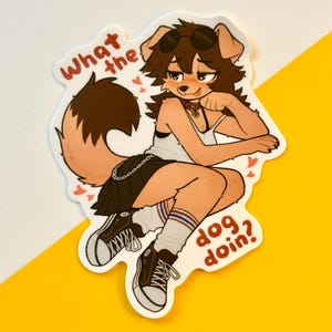 以下が含まれることがあります： 茶色の毛並みをした犬のようなキャラクターが描かれたステッカー。サングラス、白いタンクトップ、黒いスカートを着用しています。「What the dog doin?」というテキストが含まれています。ステッカーは白い縁取りと黄色の背景です。