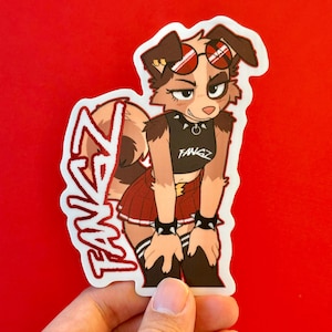 May include: A sticker featuring a cartoon dog with brown and tan fur, wearing sunglasses, a black crop top with "FANGZ" text, and a red pleated skirt. The sticker has the word "FANGZ" in a stylized font.