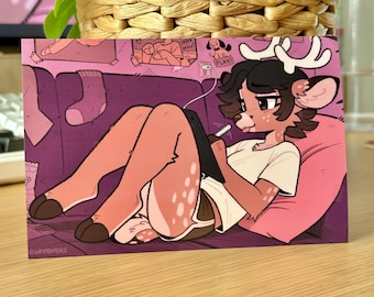 Puede incluir: Ilustración de un personaje parecido a un ciervo con cuernos, con una camiseta blanca y pantalones cortos, tumbado en una almohada rosa. El personaje está usando una tableta con un lápiz óptico. El fondo presenta un sofá morado y varios objetos.