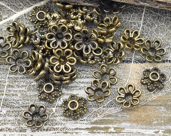 May include: A pile of antique gold-toned metal flower-shaped bead caps. The bead caps are scattered on a white, textured surface.