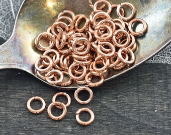 May include: A pile of rose gold jump rings in a silver spoon. The jump rings are small and round, and they are perfect for jewelry making.