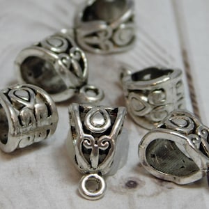 May include: Five silver-toned metal bead caps with intricate floral designs. The caps have a round opening and a loop at the top for attaching to jewelry.