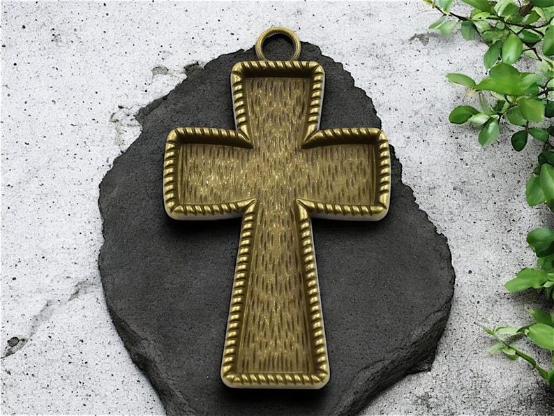 May include: A gold-toned metal cross pendant with a rope-like border. The cross is designed to be filled with resin or other materials.