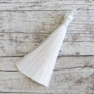 May include: A white tassel with a long, flowing fringe. The tassel is made of soft, silky fibers and has a simple, elegant design.