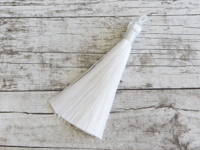 May include: A white tassel with a long, flowing fringe. The tassel is made of soft, silky fibers and has a simple, elegant design.