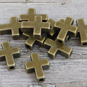 May include: A group of ten antique gold-toned metal cross charms. The charms are approximately 2.5 cm in size and have a hole for stringing.