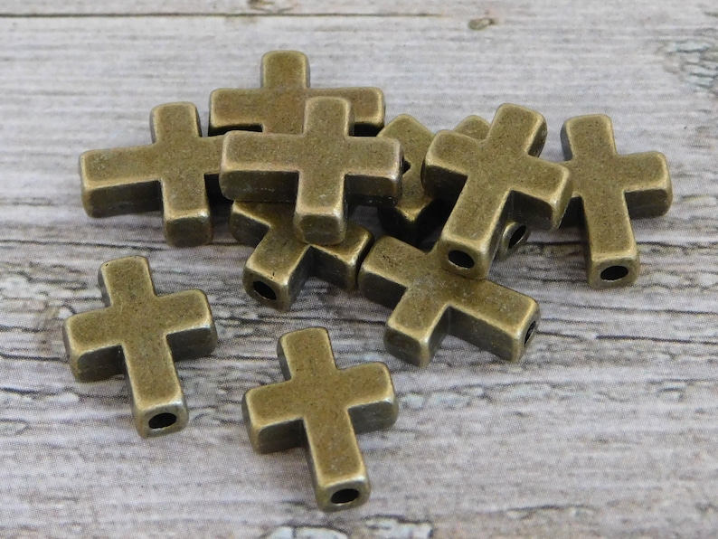 May include: A group of ten antique gold-toned metal cross charms. The charms are approximately 2.5 cm in size and have a hole for stringing.