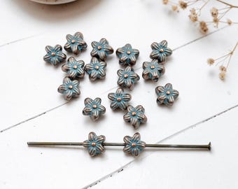May include: A collection of small, five-petaled flower-shaped beads with a copper-toned finish and teal-colored patina in the recessed areas. Two of these beads are threaded onto a long, thin, dark metal headpin.