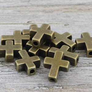 May include: A pile of antique gold metal cross charms. The charms are approximately 2.5 cm in size and have a hole in the top for stringing.