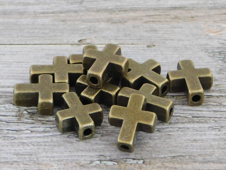May include: A pile of antique gold metal cross charms. The charms are approximately 2.5 cm in size and have a hole in the top for stringing.