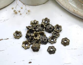 May include: A collection of small, antique bronze-colored metal bead caps shaped like six-petaled flowers. Each piece features a central circular hole and a textured, beaded edge detail, designed to sit over beads in jewelry making projects.
