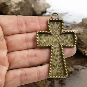 May include: A gold-toned metal cross pendant with a textured surface and a rope-like border. The cross has a loop at the top for hanging.